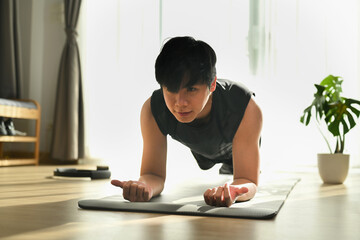 Fototapeta na wymiar Fitness man doing plank exercise on mat during morning training at home.