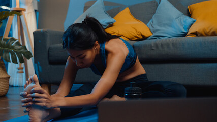 Young Asia lady in sportswear exercises doing work out and using laptop to watch yoga video...