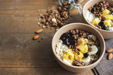 Oatmeal with pineapple, banana and chocolate granola in beige plates on a brown wooden table. A hearty healthy breakfast. A place for text.