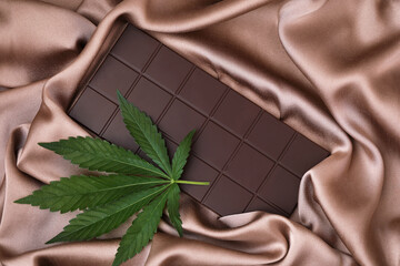 Organic Marijuana Pieces of  Dark Chocolate with CBD cannabis and dry green hemp leaves. A bar of...