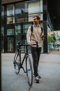 Stylish young man standing outside with his bicycle and using phone