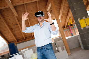 Man, builder with blue shirt looks at the conversion, extension of his loft with virtual 3d glasses and is on the construction site