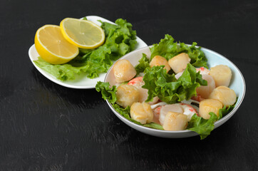 Fried scallop with boiled shrimp tail with lettuce leaves and lemon in a ceramic plate on a dark background.