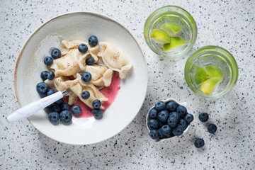 Above view of vareniki or dumplings with cottage cheese and bilberries, horizontal shot on a beige stone background