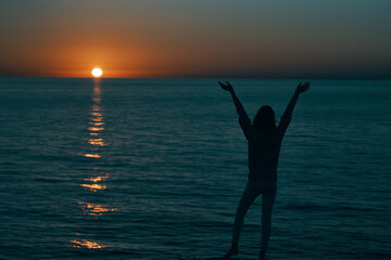 woman in the mountains at sunset near the sea raised her hands up