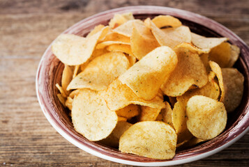 heap of potato chips in bowl on wooden background