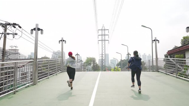 Asian woman friends in sportswear jogging together in the city. Healthy female athlete teamwork enjoy outdoor lifestyle activity do sport training workout fitness exercise running in summer morning.