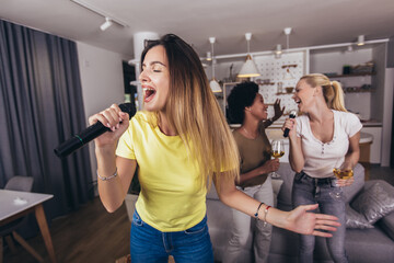 Young womanl singing into microphone at home party having fun. Bachelorette party, karaoke, music concert and holidays concept