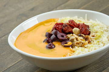 Appetizing cream soup with various cheeses, hazelnuts, olives and sun-dried tomatoes in a white plate on a wooden background