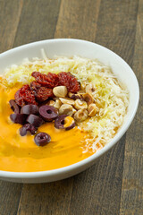Appetizing cream soup with various cheeses, hazelnuts, olives and sun-dried tomatoes in a white plate on a wooden background