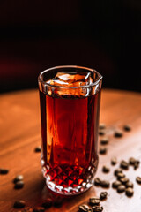 A cocktail in a collins highball glass with an ice spear, coffee beans around, on a wooden table,...