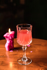 A pink cocktail in a beautiful crystal glass, a candle, on a wooden table, at the bar.