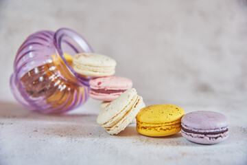 Colorful macaroons pour out of a glass lilac vase.