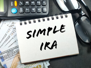 Business concept.Text SIMPLE IRA with glasses,calculator and banknote on black background.