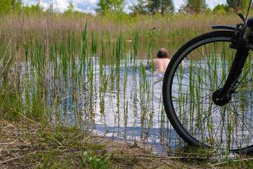 Bicycle wheel on a forest lake background. Athletic man swims in the lake.