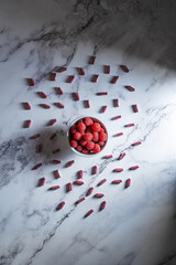 Flat lay bright product photography of strawberries and powder capsules on a white marble board. Natural medicine and herbal supplement therapy concept.