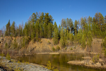 Obraz premium The beauty of a huge career in the Urals. Pine trees grow on quarries of a rocky quarry, mine workings, water at the bottom. Reddish rocks