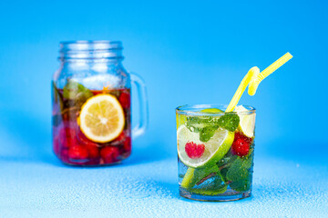 Cocktail in glass with lemon, lime, mint and raspberries on aqua blue background.
