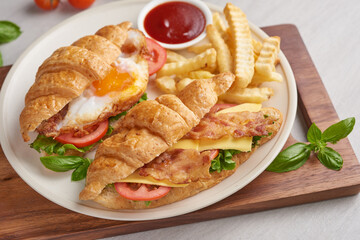 two croissant sandwiches on wooden table, top view, Sandwich with bacon, fried egg. Ham, cheese, bacon, fried egg, tomato, french fries and lettuce served in a plate.