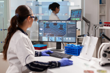 Biologist doctor checking DNA informations typing on pc in modern equipped laboratory. Scientists examining vaccine evolution in medical lab using high tech, chemistry tools for scientific research.