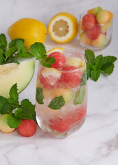 Refreshing summer citrus cocktail with lemon, watermelon and melon with mint and ice cubes in glass, homemade fresh fruit, fruit drink for healthy concept, selective focus.
