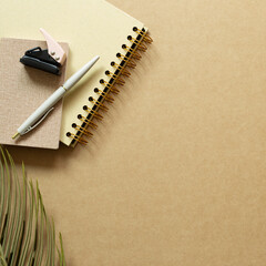 Notebook, pen, stapler, green leaf on kraft brown paper background. flat lay, top view, copy space