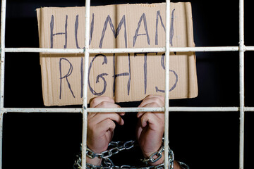 concept human rights freedom of speech hands shackled with an iron chain hold a cardboard sign with the inscription human rights behind an iron grate