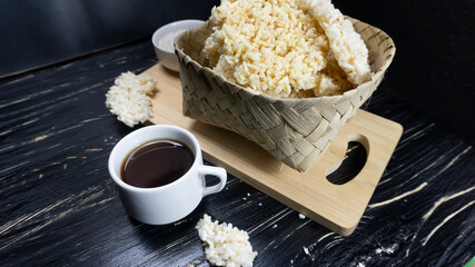 Rengginang or chips made from traditional glutinous rice from Indonesia are placed in a container made of bamboo against a background of a black wooden table.