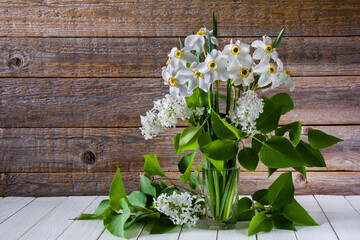 Bouquet of white flowers of daffodils and lilacs in a glass on a wooden table. Still life