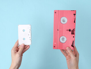 Hands holding retro video and audio cassette on blue background