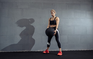 Sportswoman doing stretching exercise with medicine ball. Muscular woman exercising fitness ball at gym