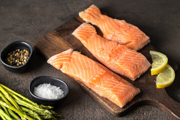 Raw salmon fillets, salt, herb , lemons and asparagus on concrete background ready for cooking.