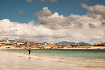 Fototapeta na wymiar Young teenager girl walking on a warm sand of Gurteen beach, county Galway, Ireland. Warm sunny day. Cloudy sky. Outdoor activity concept. Beautiful Irish scenery in the background