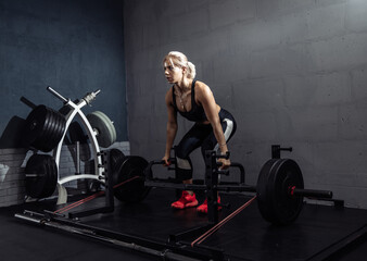 Fototapeta na wymiar Woman exercising with heavy weights in gym. Fit female doing deadlift workout with barbell