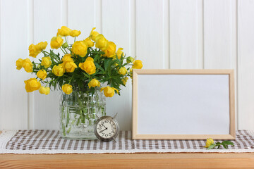 empty rectangular frame and yellow spring flowers in a glass vase.