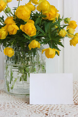 blank card and yellow spring flowers in a glass vase.