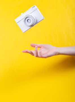 Hand and Levitating white film camera on yellow background. Minimalistic still life. Concept art