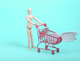 Puppets holding mini shopping trolley with glasses on blue background. Shopping concept