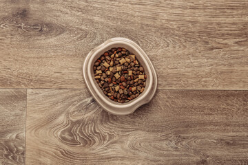 Plastic bowl with cat food on wooden floor. Top view
