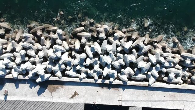Top-down view of small waves lapping against Dolos tetrapods on one side and concrete walkway on other side camera moving up and away Aerial Video