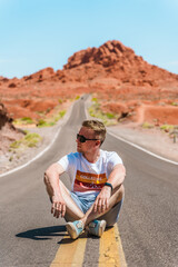 Naklejka na ściany i meble A young man sits on a scenic road in Valley of fire, Nevada. Valley of fire, USA - 18 Apr 2021
