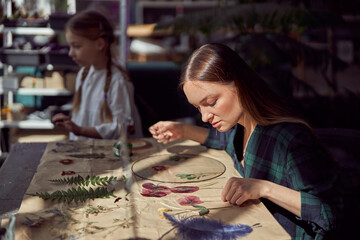 Fototapeta premium Flourist shop with different kinds of dryed flowers. Young happy confident specialist is working with her female kid.