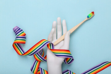 Hand holding Toothbrush and rainbow tape on a blue background. Lgbt concept
