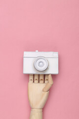Wooden hand holding White painted camera on pink background. Minimalism