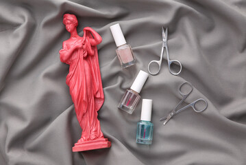 Antique pink statue, bottle of nail polish, scissors on gray silk background. Beauty concept