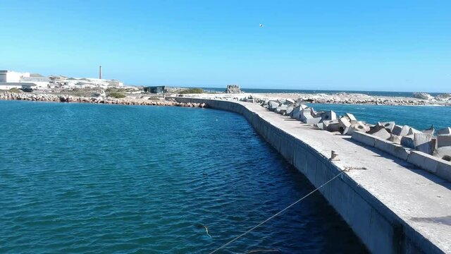 Breakwater of the small harbor with Dolos tetrapods on one side and concrete walkway on other side Bird Island in the distance camera moving forward along the breakwater Aerial Video.