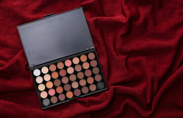 Bright make up eye shadow pallete on red silk background. Beauty still life.