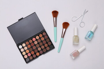 Beauty products on a white background. Make up eye shadow palette, makeup brushes, scissors and nail polish. Top view. Flat lay