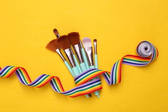 Makeup brushes with rainbow tape on yellow background. Beauty layout.