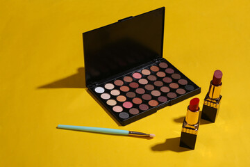 Women's accessories. Beauty products on blue background. Make up eye shadow palette, makeup brushes and lipstick.